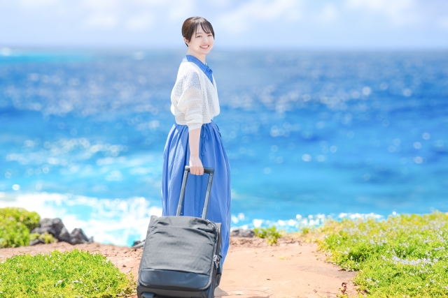 海バックでスーツケースを転がす女性